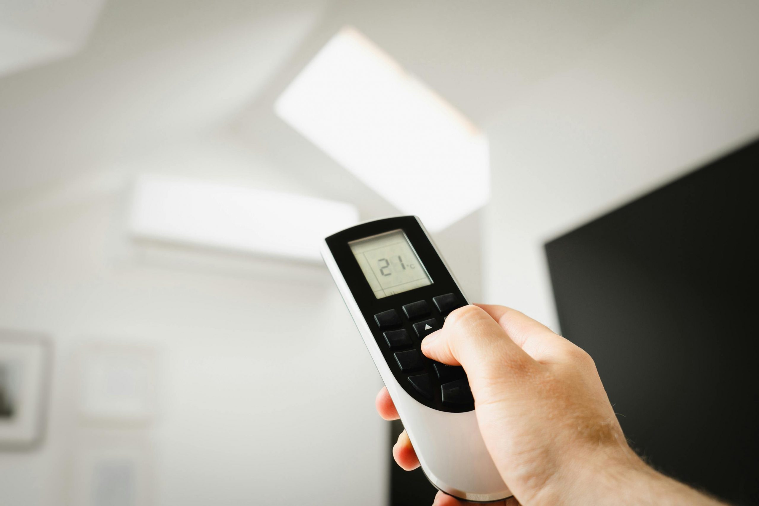 hand holding a remote control, pointing it at a wall-mounted air conditioning unit