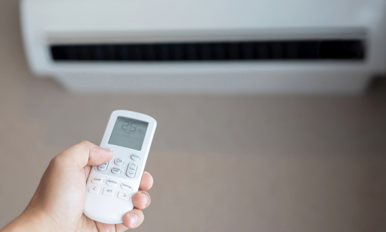 hand holding a remote control, pointing it at a wall-mounted air conditioning unit