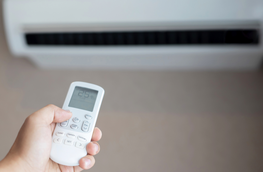 hand holding a remote control, pointing it at a wall-mounted air conditioning unit
